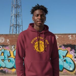 Young man in a maroon hoodie standing in front of a graffiti wall and a tall tower.